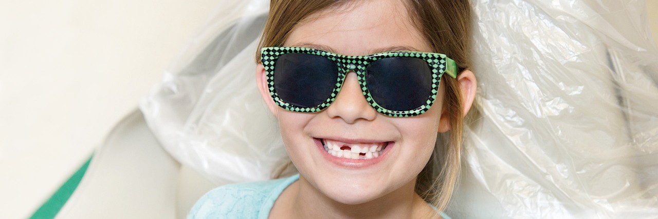 Photo of a smiling child in a dentist chair showing dental care provided by dentists (DDS, DMD) and registered dental assistants.