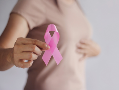 Woman holding a pick ribbon and touching breast to rpomote breast cancer screenings