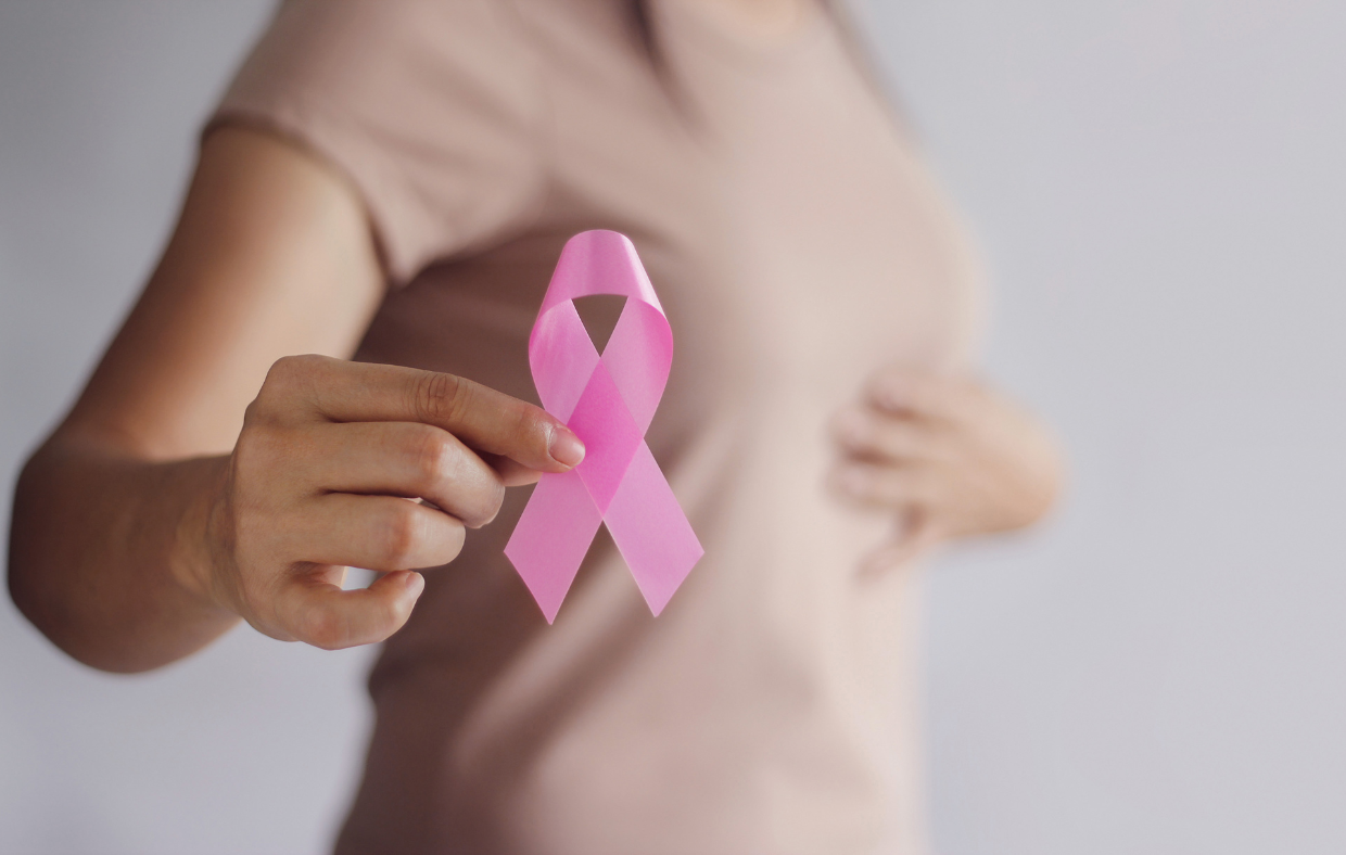 Woman holding a pick ribbon and touching breast to rpomote breast cancer screenings